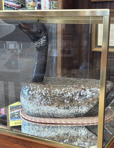 A wooden duck sculpture in a glass display case with a brass frame.