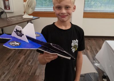 Young person holding a blue airplane model indoors.