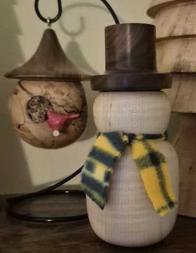 Wooden snowman with a top hat and scarf next to an acorn-shaped ornament with a red bird.