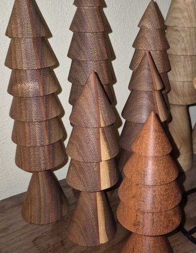 Wooden sculptures resembling stylized pine trees made of stacked conical sections, displayed on a wooden surface.