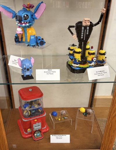 A display case containing multiple LEGO models, including Stitch, Gru with minions, a red gumball machine, and assorted mini figures.