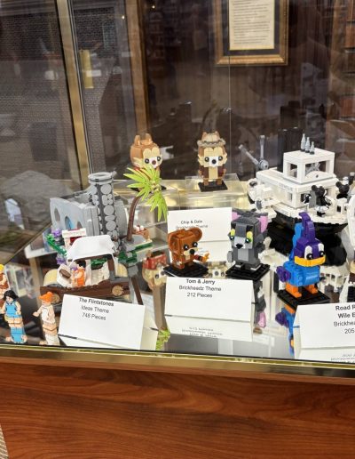 Display case featuring LEGO sets of cartoon characters including "The Flintstones," Chip and Dale, Tom and Jerry, and Road Runner & Wile E. Coyote, with labels listing details.