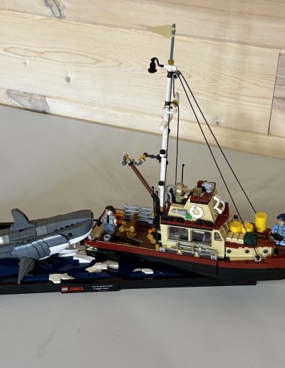 A detailed LEGO model of a fishing boat with a shark, featuring two minifigures and wave elements on a blue base.