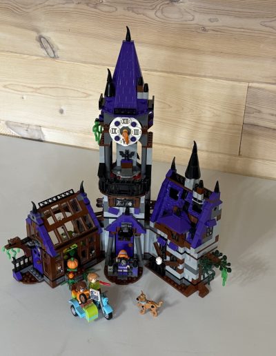 A LEGO haunted house set with a tall purple tower and two smaller buildings in front, accompanied by Scooby Do mini-figures.