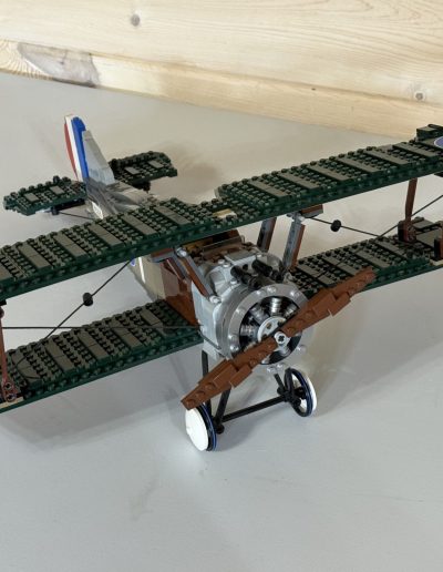 A detailed model of a green and silver biplane made from LEGOs, with circular blue and red markings on the wings, on a light-colored surface.
