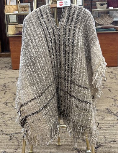 Gray-and-cream fringed woven textile displayed over a chair in front of museum cases.