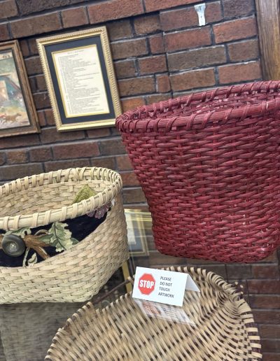 Display case containing several woven baskets, including a large red basket and a smaller tan basket, with a “STOP” artwork warning sign.
